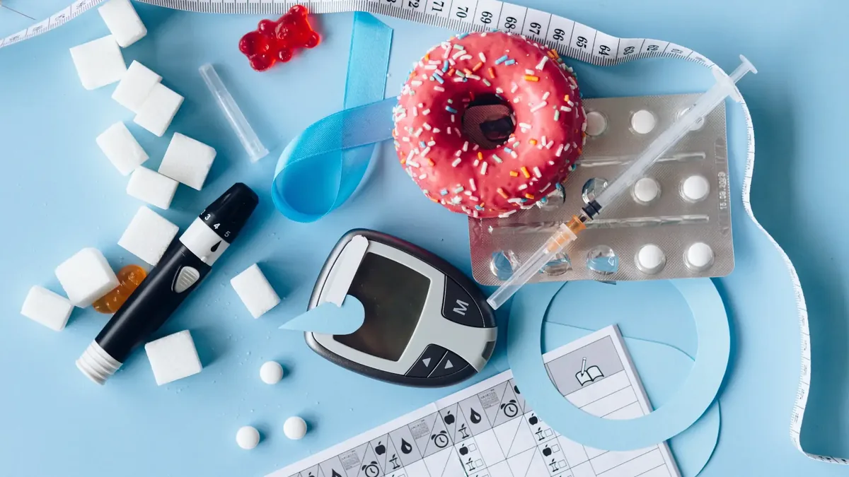 Blutzuckermessgerät, Stechhilfe, Insulinspritze, Zuckerwürfel und ein Donut auf hellblauem Grund